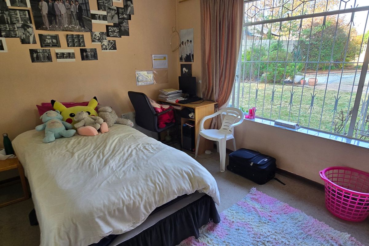 A functional bedroom featuring a large window with security bars, overlooking the garden area, and including a built-in cupboard.