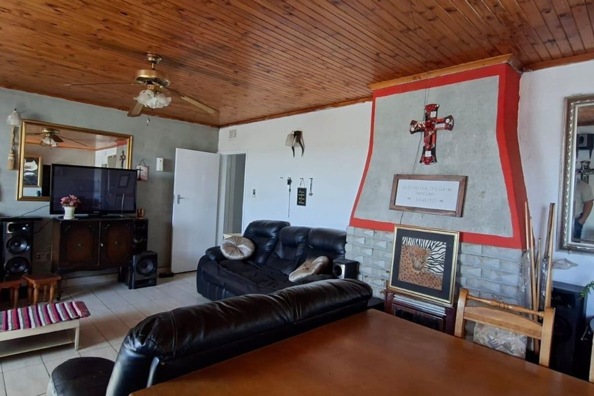 Living room featuring a prominent brick fireplace, timber-clad ceiling, and tiled flooring, offering a dated aesthetic with potential for modernization.