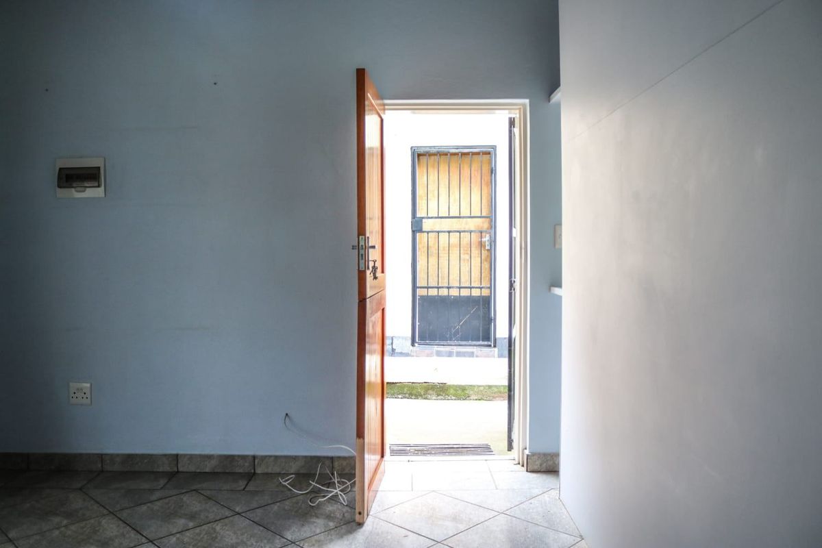 An empty entry area featuring tiled flooring, a wooden door, and a security gate leading to the exterior.