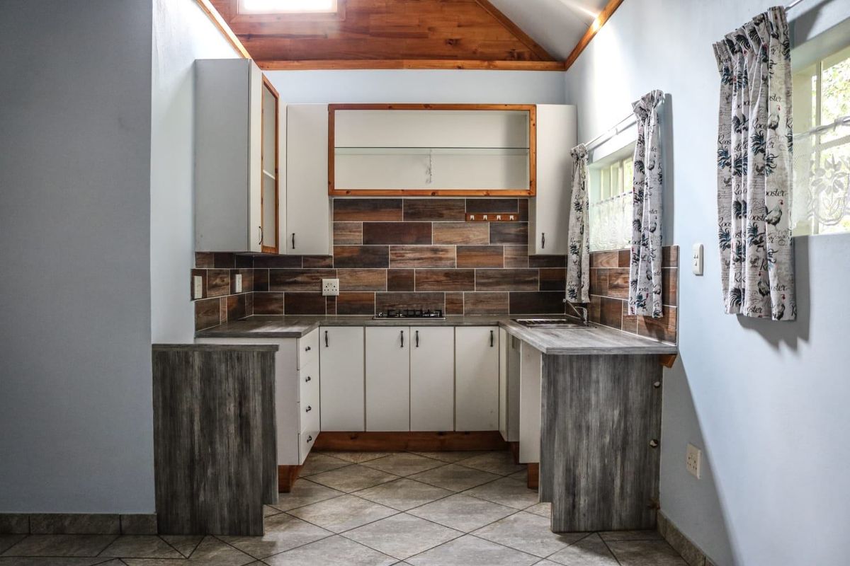 A compact kitchen featuring built-in cabinetry, a tiled backsplash, a cooktop, and a distinctive timber-paneled vaulted ceiling.