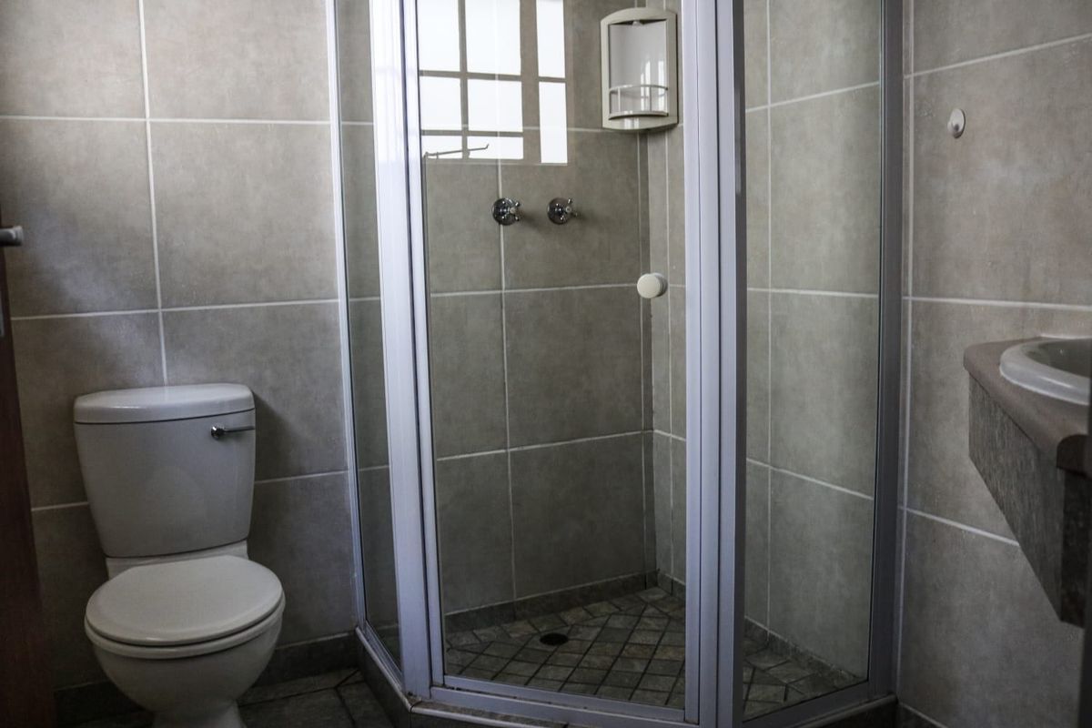 A functional bathroom featuring a corner shower enclosure, standard toilet, and tiled finishes throughout.
