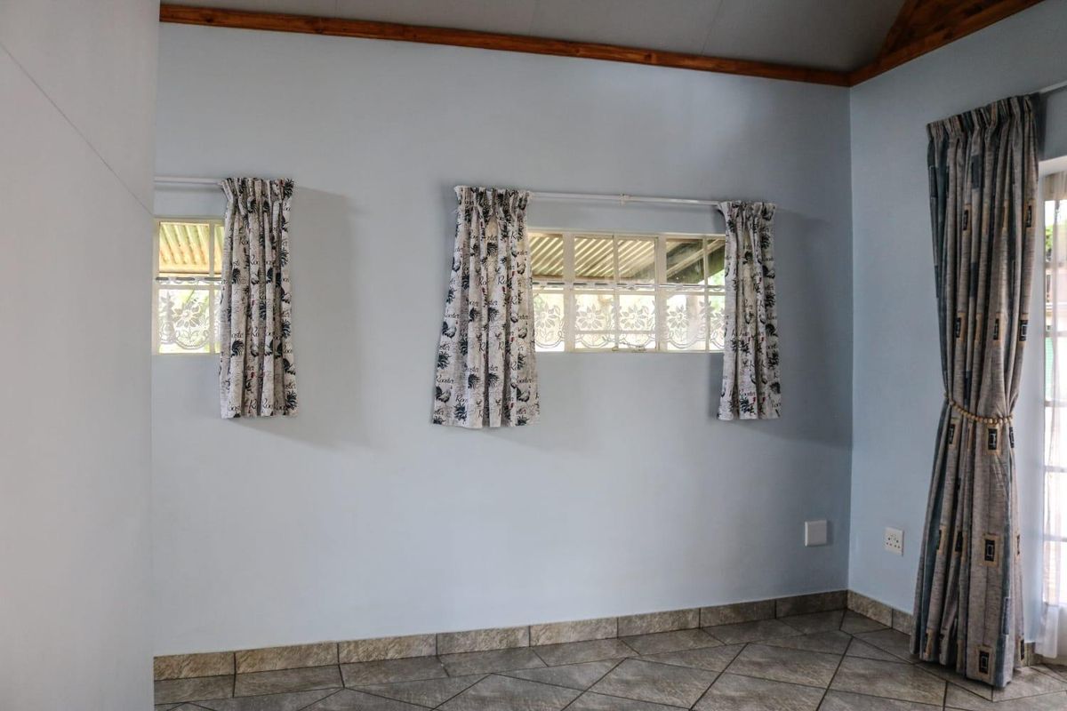 A bright, empty bedroom featuring tiled flooring, timber ceiling trim, and multiple windows allowing for natural light.