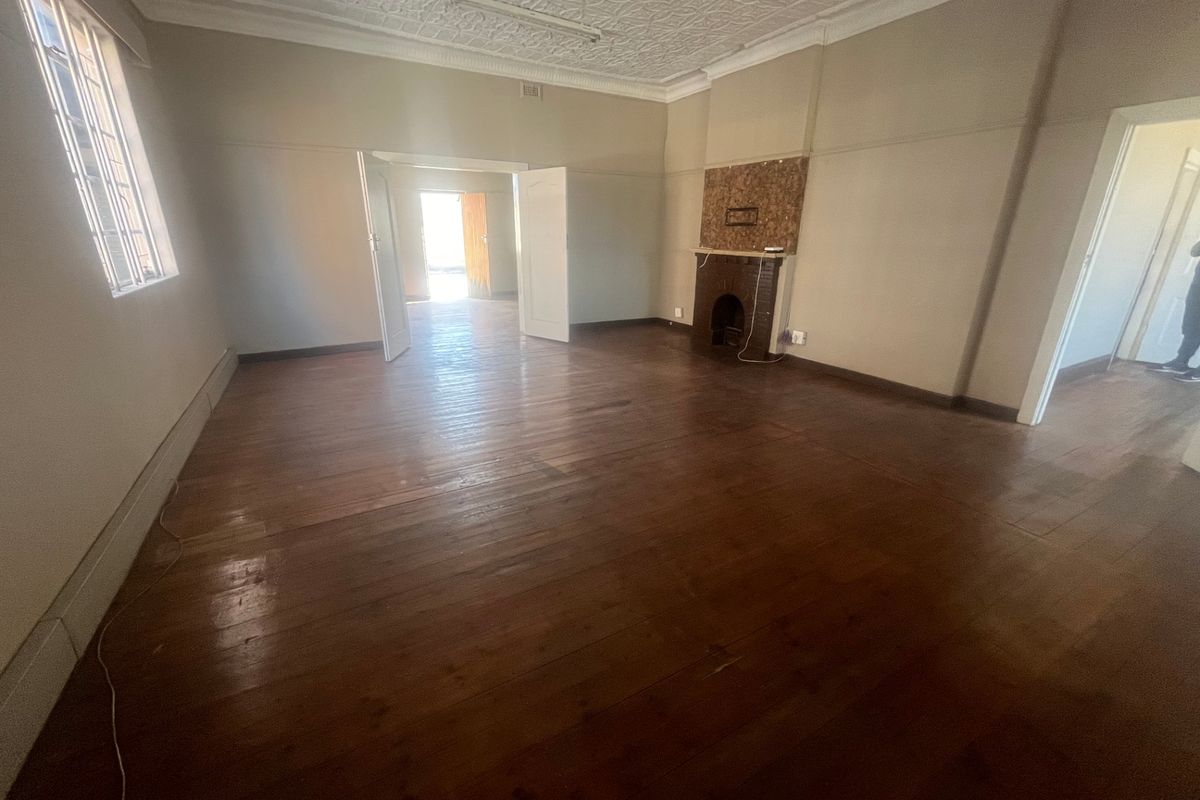 Spacious living area featuring original hardwood flooring, an ornate pressed metal ceiling, and a traditional brick fireplace, offering a classic character aesthetic.