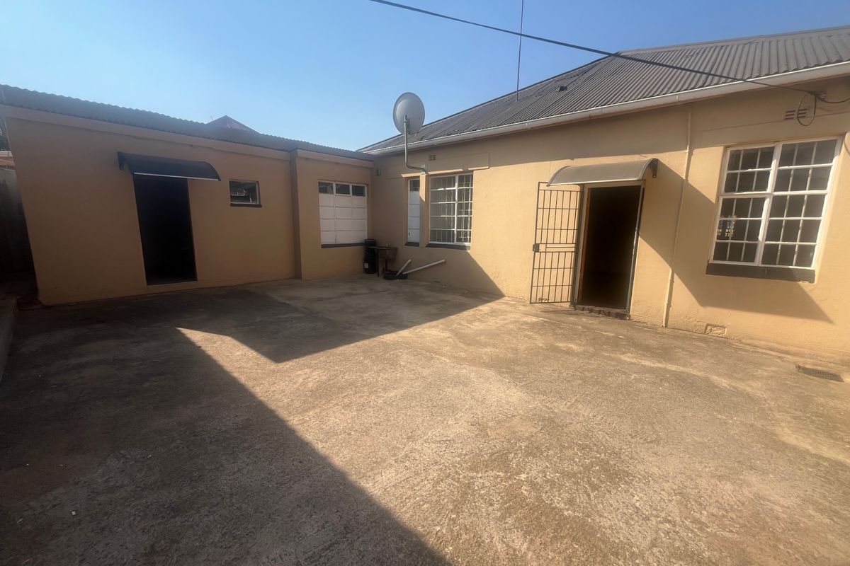 A paved rear courtyard area featuring security gates, awnings, and access points to the main building structure.