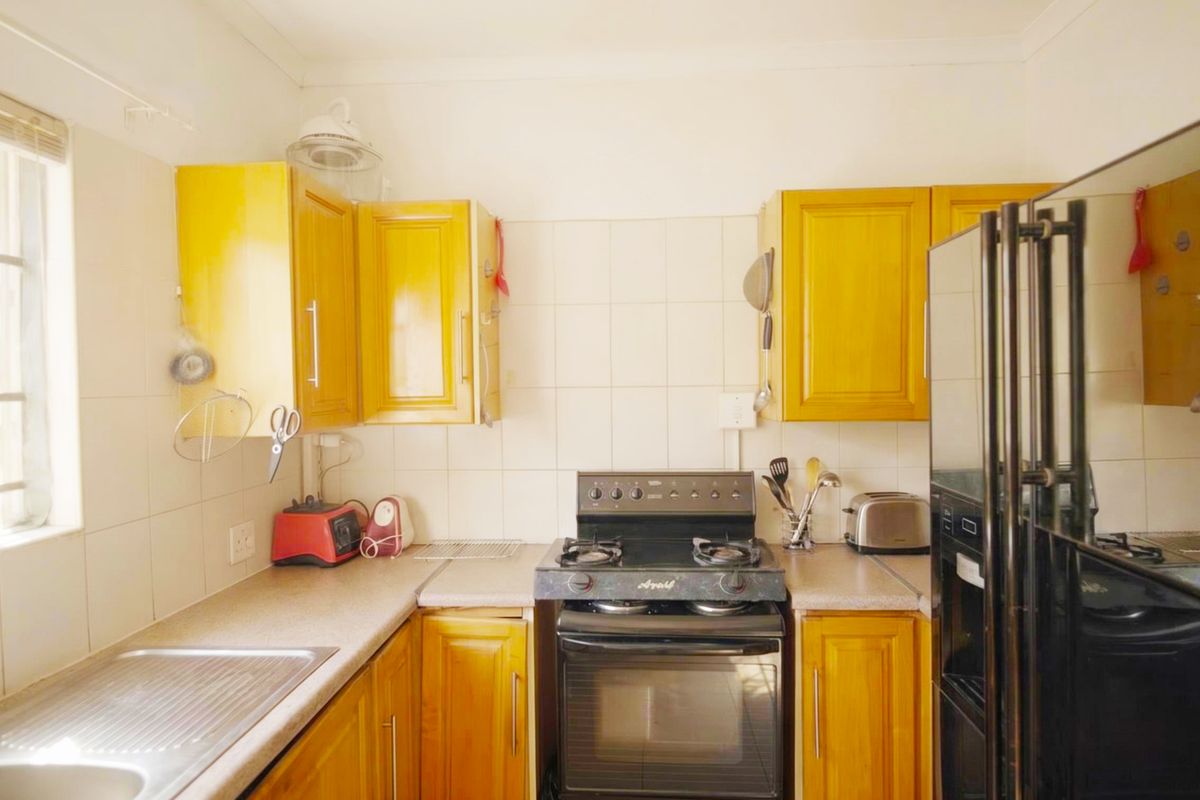 A functional kitchen featuring wooden cabinetry, laminate countertops, a tiled splashback, and a freestanding gas oven and hob.