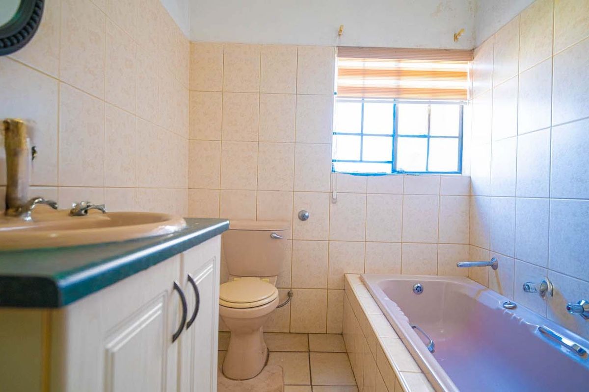 A dated bathroom featuring a built-in vanity, toilet, and bathtub with tiled finishes throughout, requiring cosmetic updates to modernize the space.