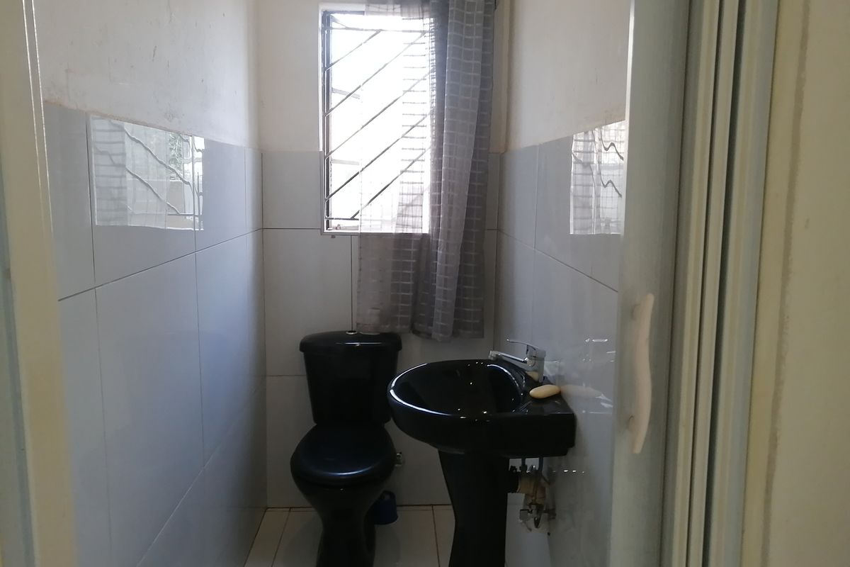 A compact bathroom featuring black sanitaryware, tiled walls, and a window with security bars.
