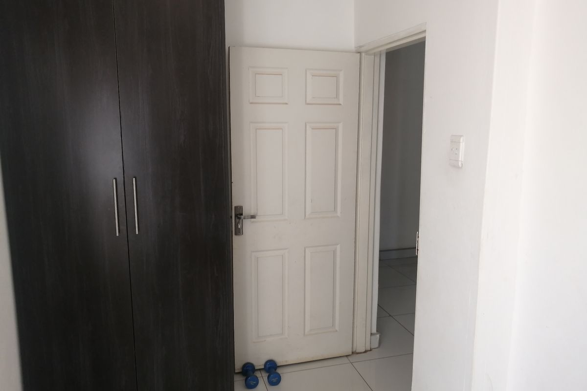 A bedroom interior featuring a dark wood-finish built-in wardrobe, white tiled flooring, and a standard internal door leading to an adjacent space.