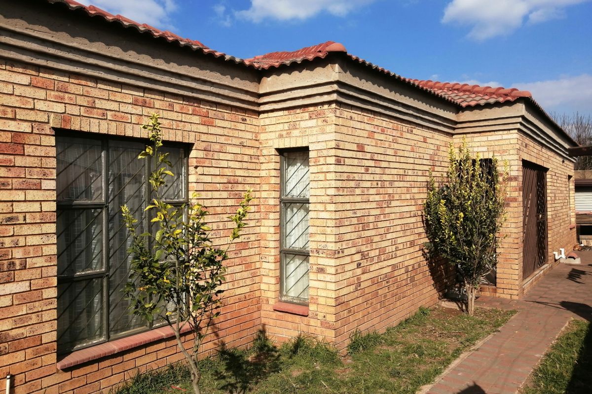 A view of the rear exterior featuring face brick walls, terracotta roof tiles, and security bars on the windows with a paved walkway.