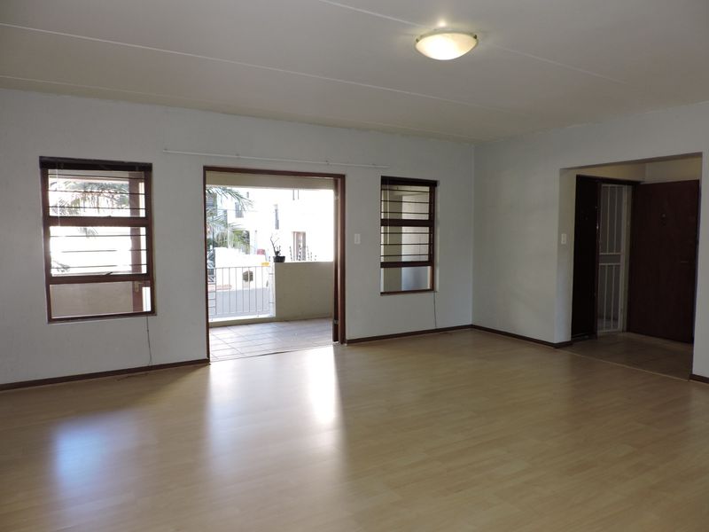Spacious, empty living room featuring light laminate flooring, large windows with security bars, and direct access to an outdoor balcony area.