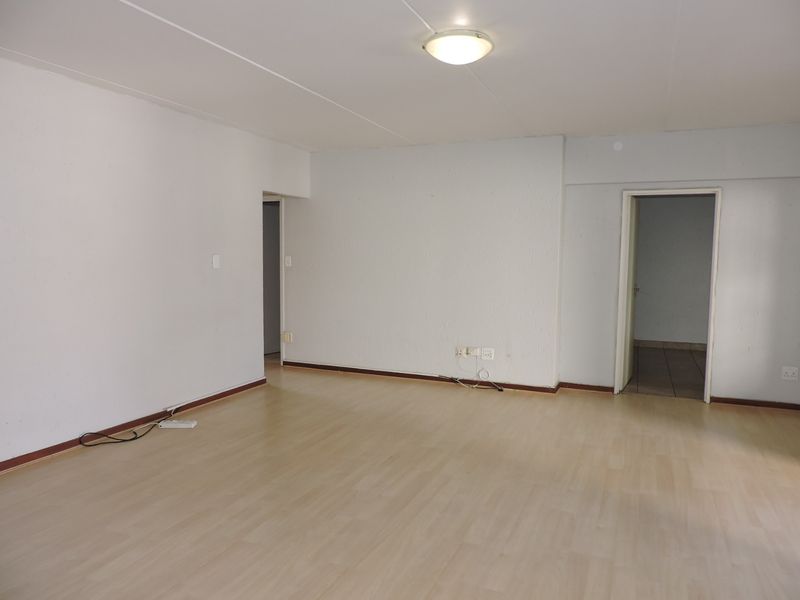A spacious, empty living area featuring light-toned laminate flooring, neutral walls, and a simple flush-mount ceiling light fixture.