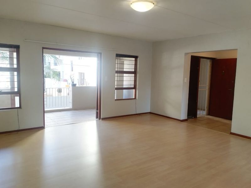 Spacious, empty living area featuring laminate flooring, neutral walls, and direct access to a private balcony through a sliding glass door.