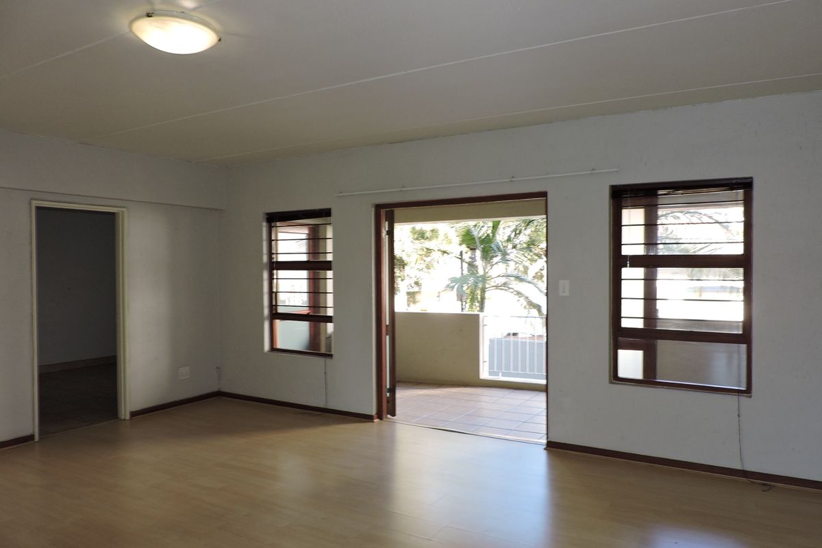 Spacious, empty living area featuring laminate flooring, neutral walls, and direct access to an outdoor balcony through a sliding door.