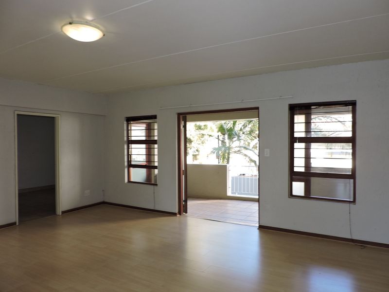Spacious, empty living area featuring laminate flooring, neutral walls, and direct access to an outdoor balcony through a sliding door.