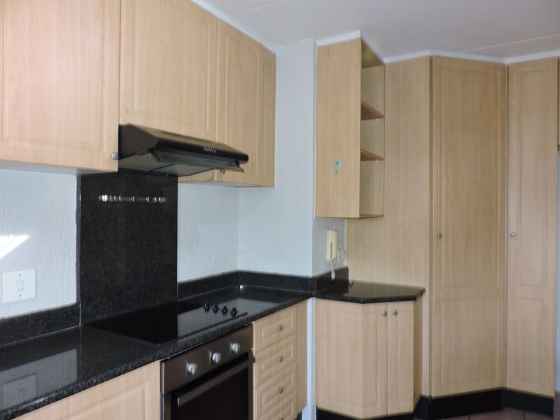 A functional kitchen featuring light wood cabinetry, dark granite countertops, a built-in oven, and an electric hob with an extractor fan.