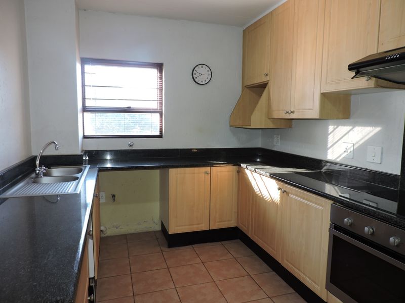 A functional kitchen featuring granite countertops, built-in oven, hob, extractor fan, and wooden cabinetry, requiring some cosmetic attention to the walls.