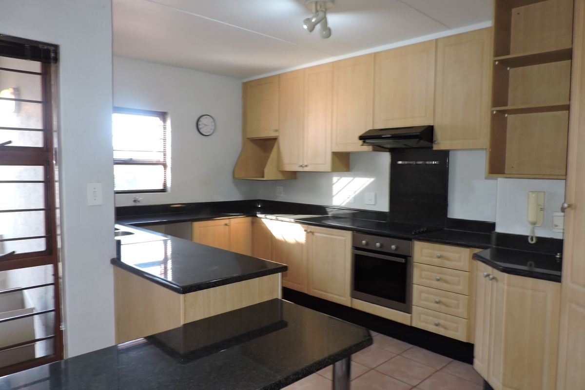 A functional kitchen featuring light wood cabinetry, dark granite countertops, built-in oven, extractor fan, and tiled flooring.