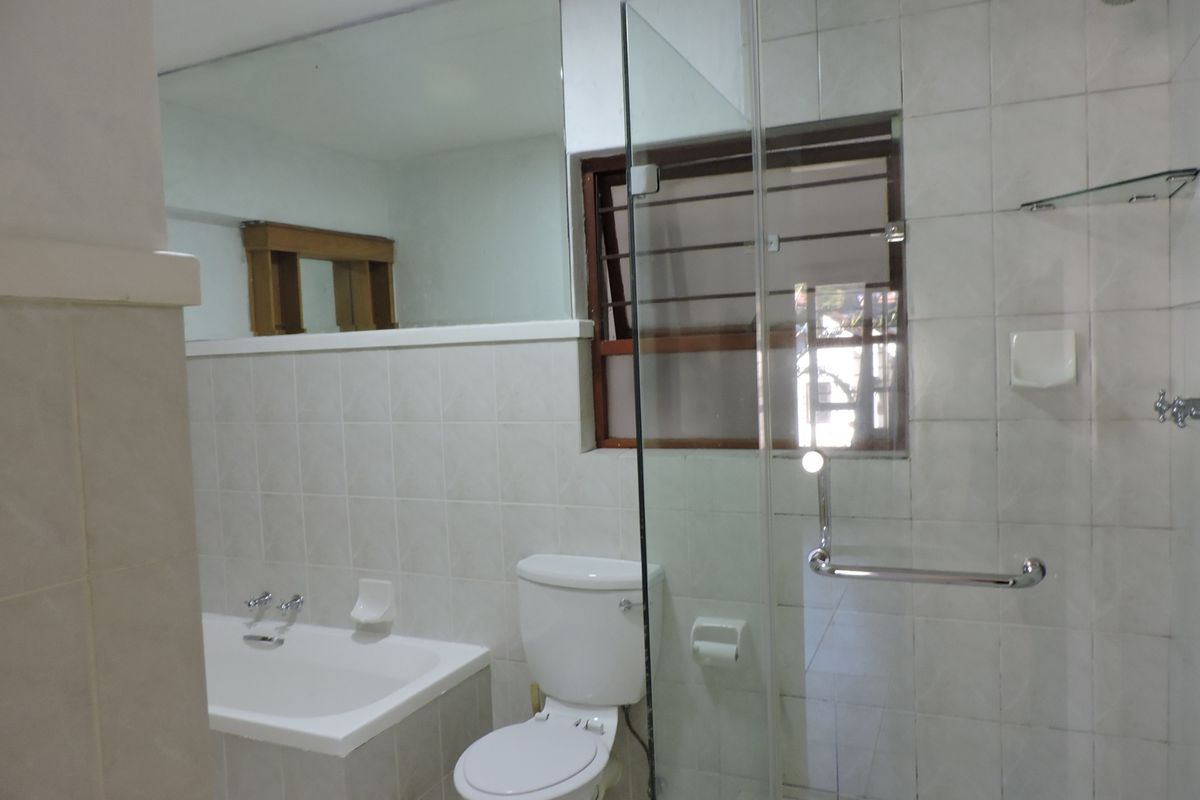 A functional bathroom featuring a built-in bathtub, a separate glass-enclosed shower, a toilet, and a large wall mirror with neutral tiled finishes.