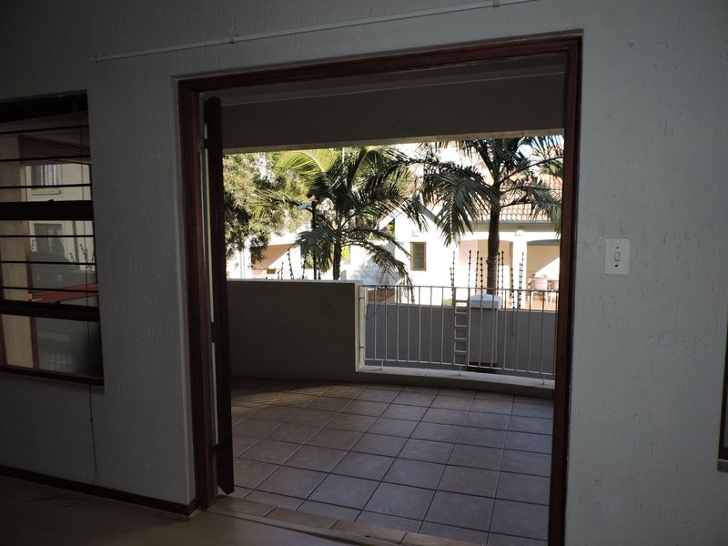 A covered balcony featuring tiled flooring and a metal balustrade, accessible through a wooden door frame from the interior living space.