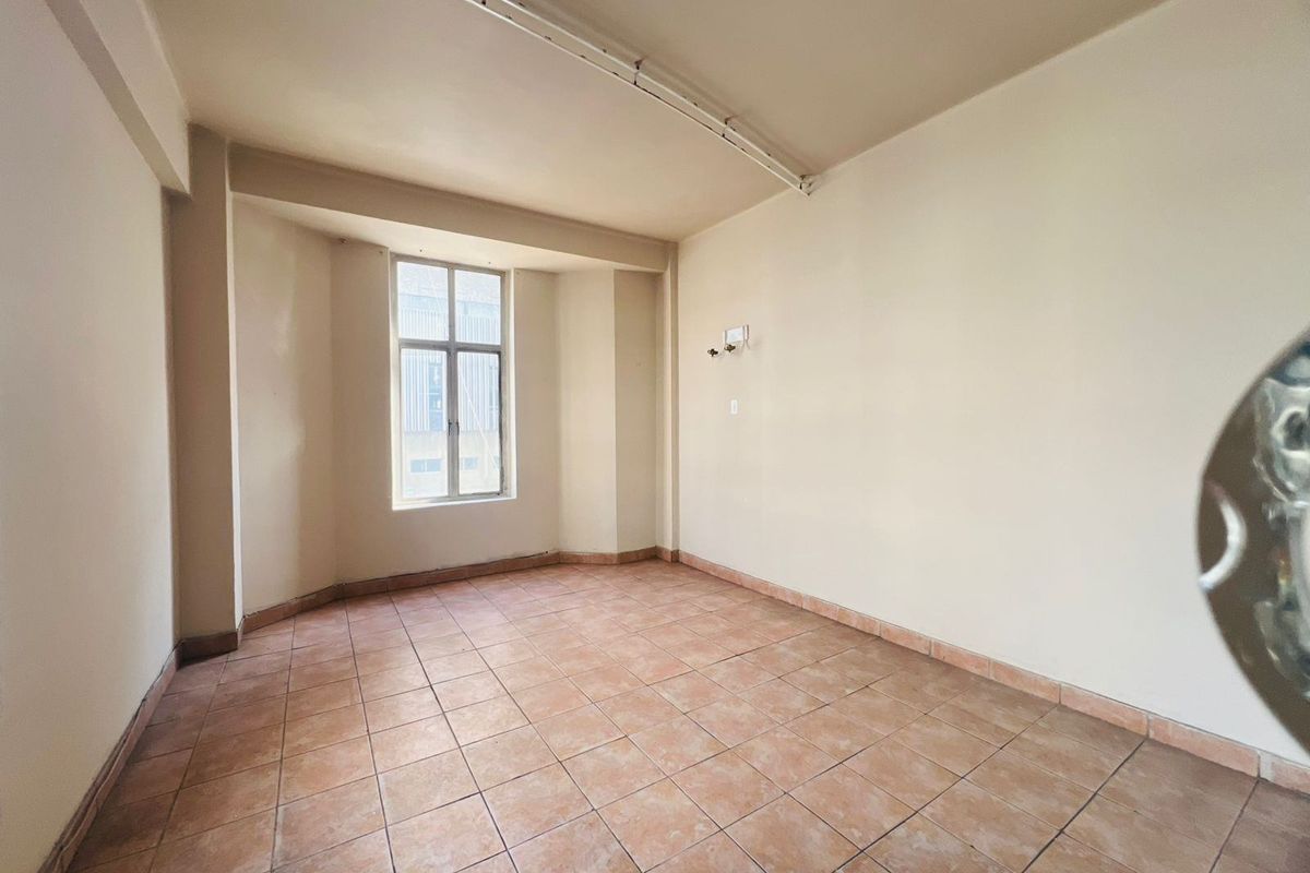 An empty, neutrally painted room featuring tiled flooring, a large window, and exposed ceiling lighting fixtures, offering a blank canvas for interior design.