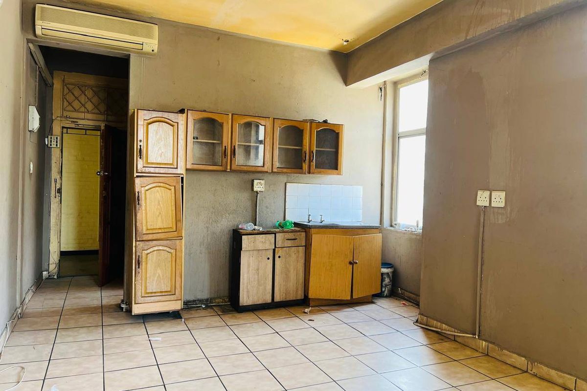 A dated kitchen area featuring basic wooden cabinetry, tiled flooring, and a wall-mounted air conditioning unit, requiring significant renovation and cosmetic updates.