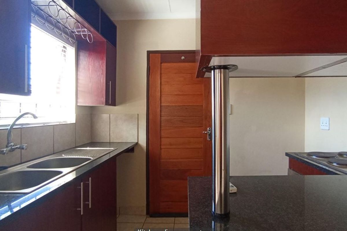 A functional kitchen featuring dark wood cabinetry, granite countertops, a double basin sink, and a built-in electric hob with tiled splashbacks.