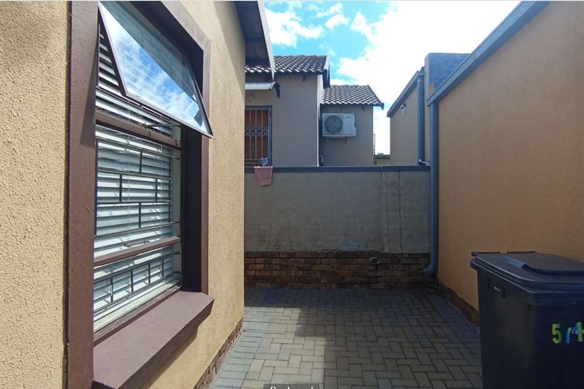 A paved rear courtyard area featuring boundary walls, security window bars, and exterior drainage infrastructure.