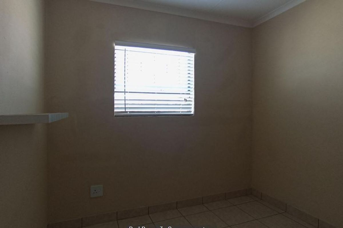 A simple, empty bedroom featuring neutral wall tones, tiled flooring, and a window fitted with venetian blinds.