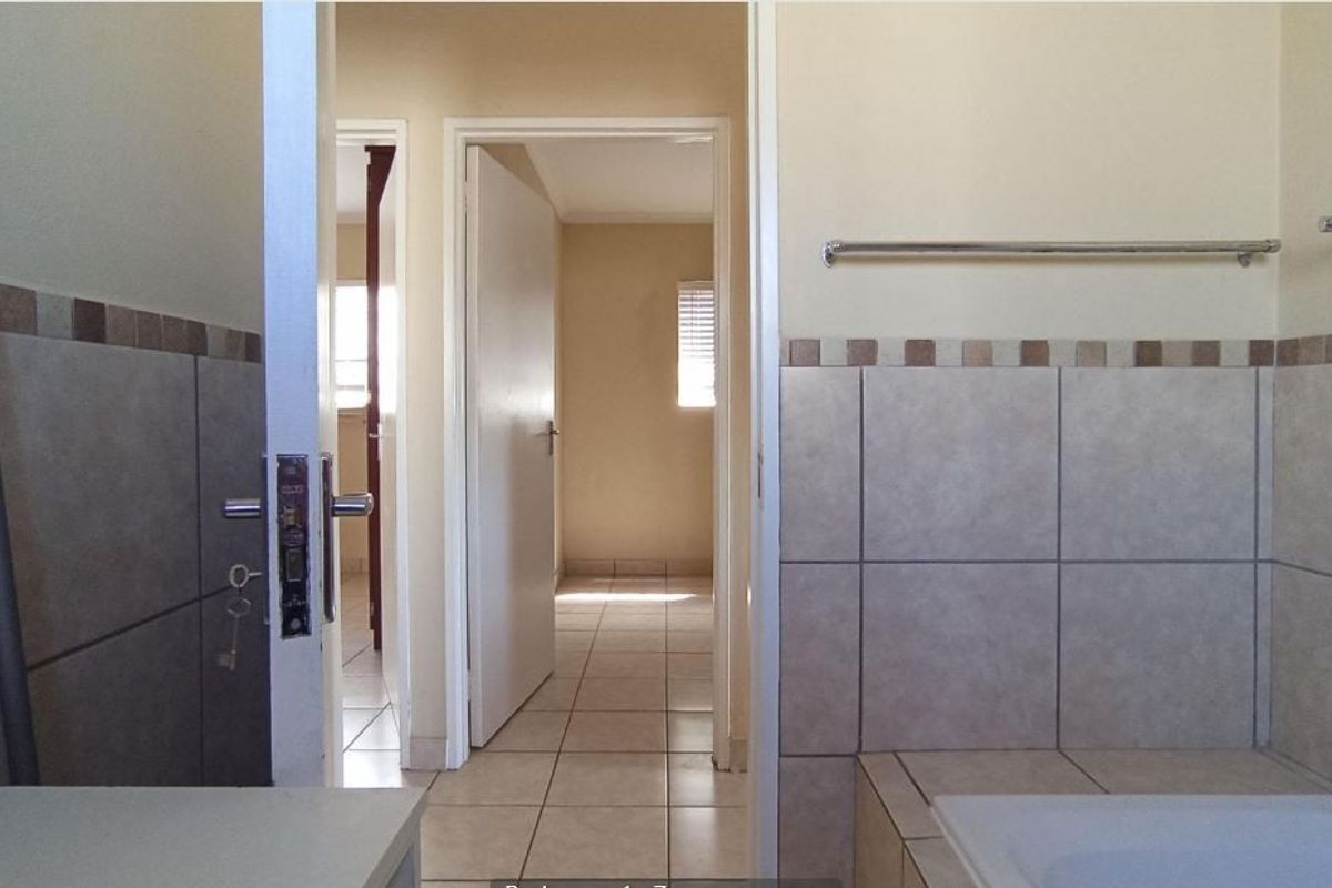A functional bathroom featuring tiled walls and flooring, with a built-in bathtub and towel rail, leading into a hallway.