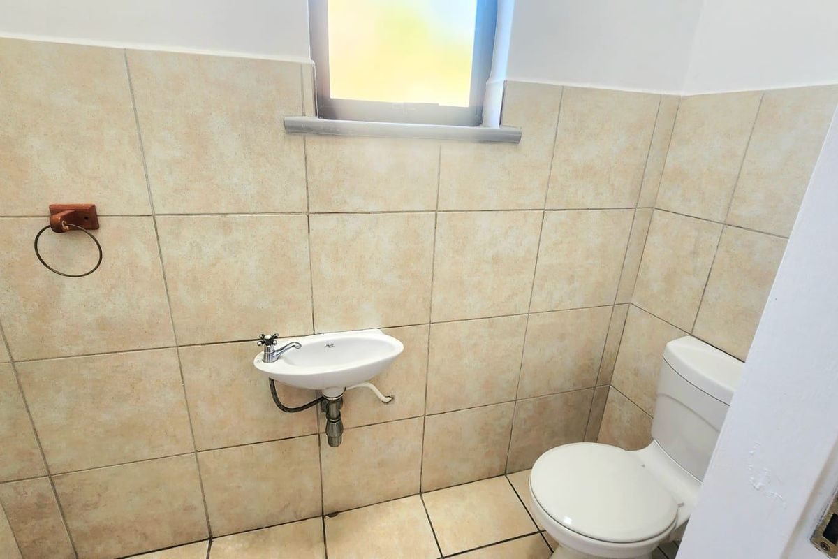 A compact commercial bathroom featuring a wall-mounted basin, standard toilet, and neutral ceramic tiling throughout.