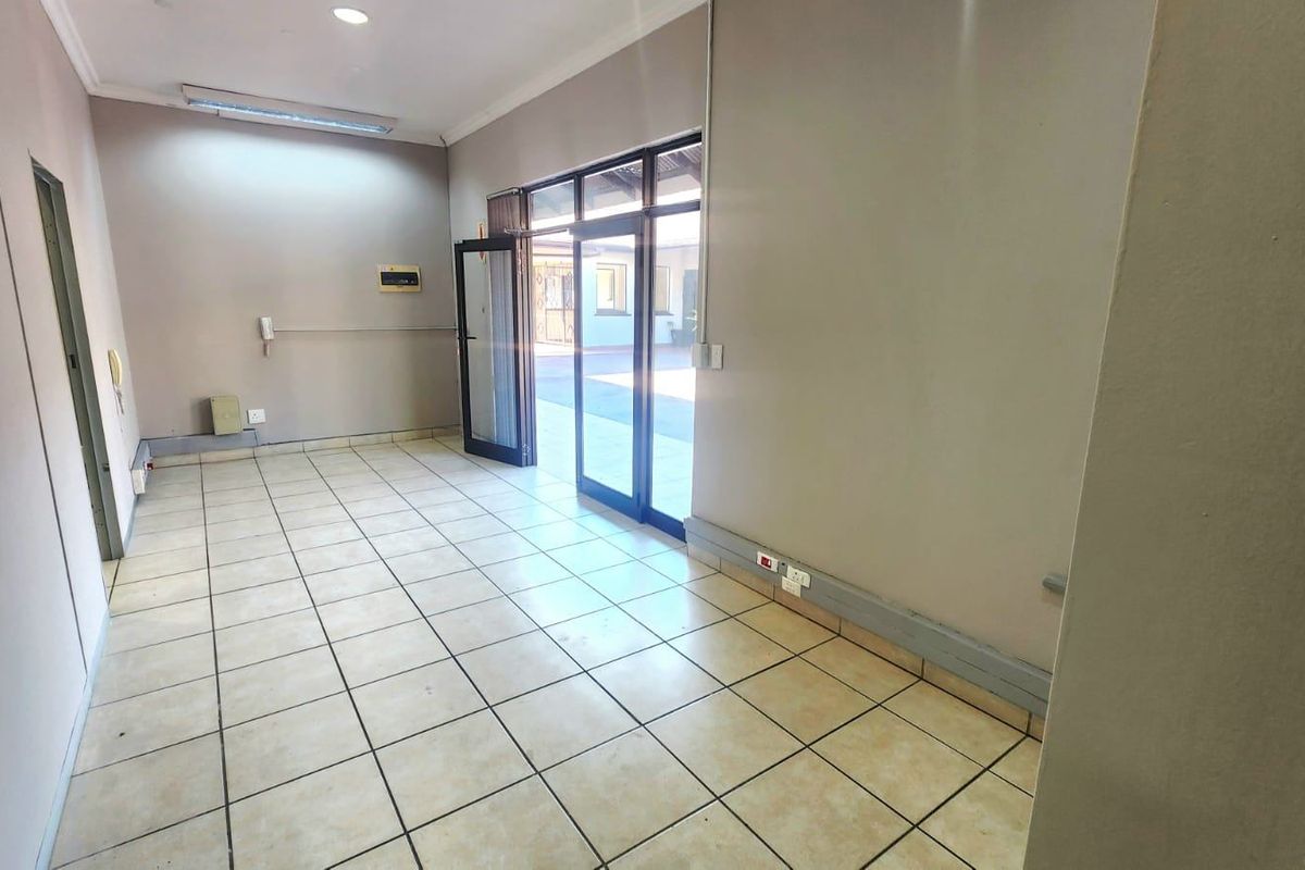 A vacant commercial office space featuring tiled flooring, recessed lighting, and direct access to an outdoor area through aluminium framed glass doors.