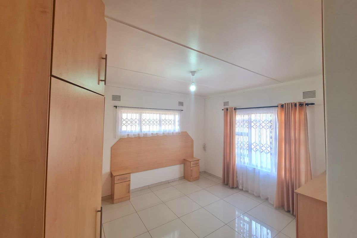 A bedroom featuring tiled flooring, built-in cupboards, and a matching built-in headboard with integrated bedside tables, complemented by security gates on the windows.