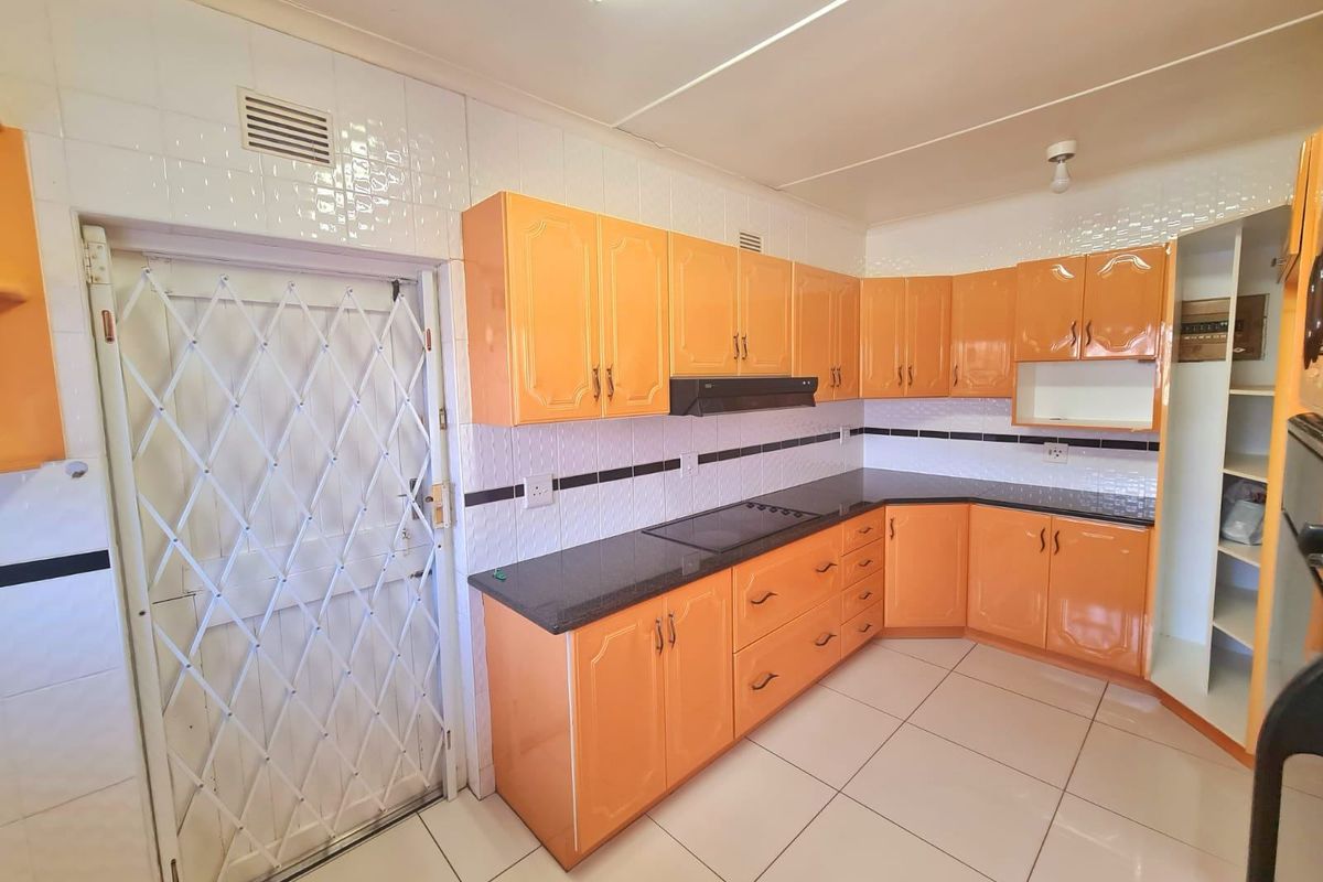 A functional kitchen featuring orange built-in cabinetry, dark countertops, an electric hob with extractor fan, and tiled flooring with a security gate.