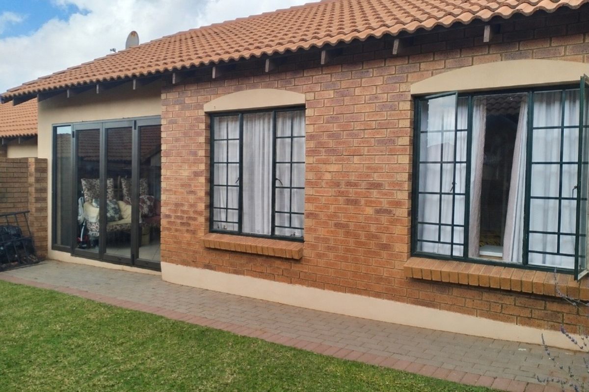Rear view of a townhouse featuring a face brick facade, tiled roof, aluminium windows, and sliding doors leading to a paved walkway and garden.