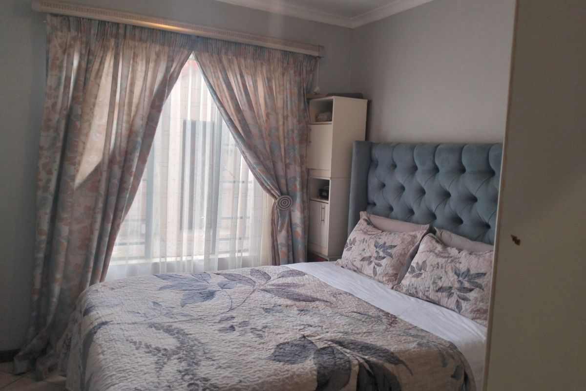 A cozy bedroom featuring tiled flooring, built-in shelving, and large windows with curtain rails, providing a comfortable and functional living space.