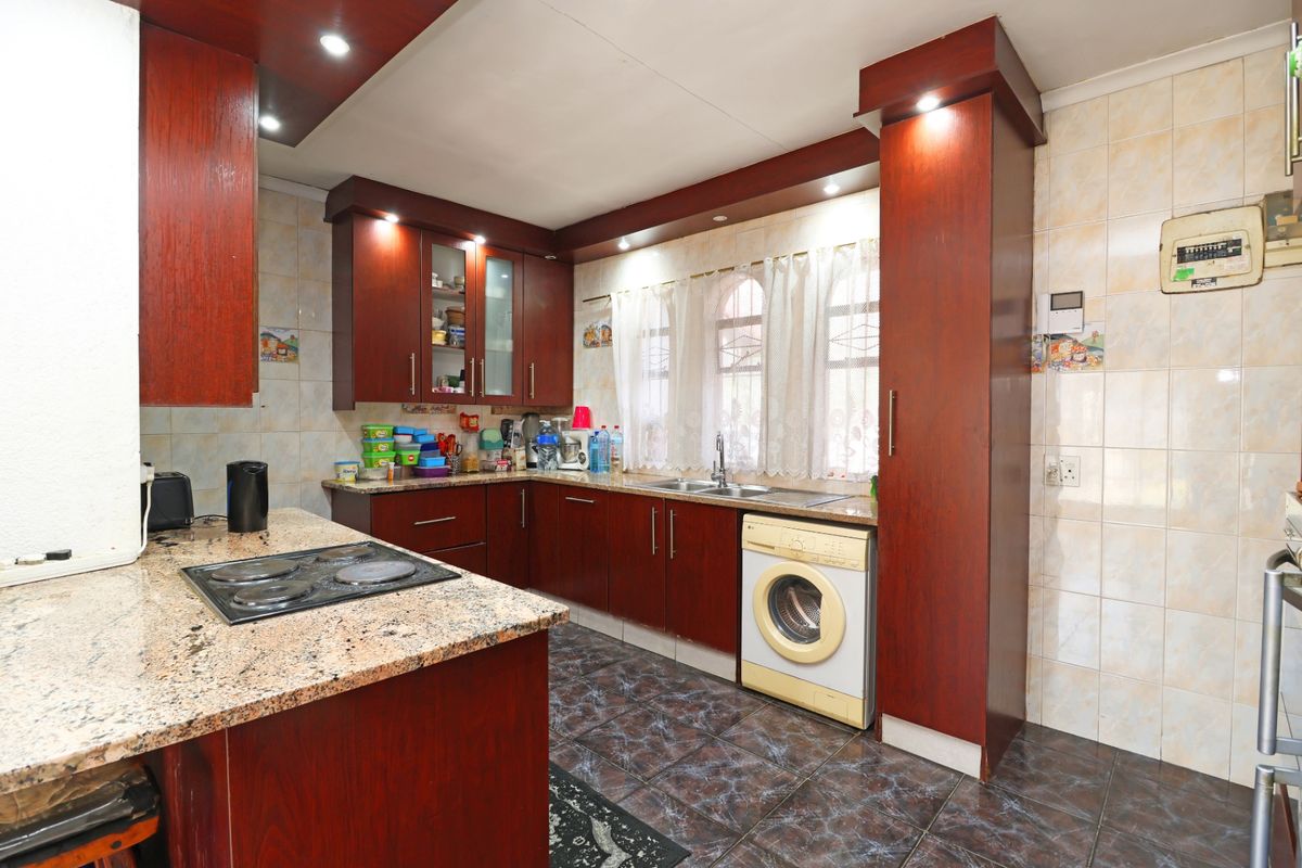 A functional kitchen featuring dark wood cabinetry, granite countertops, an electric hob, and tiled finishes with integrated laundry plumbing.