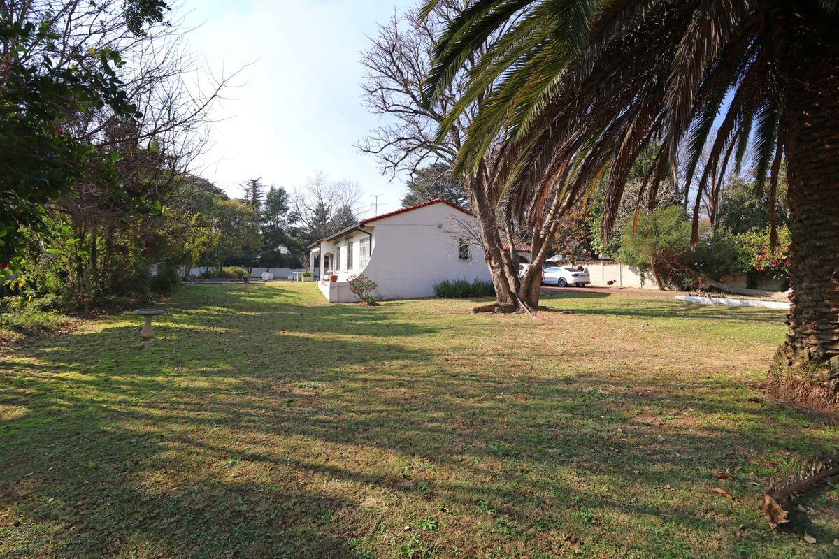 A view of the rear garden and side elevation of the house, featuring a spacious lawn and mature trees.