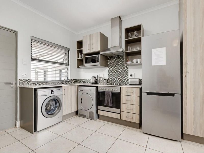 Modern kitchen featuring light wood-finish cabinetry, mosaic tile backsplash, stainless steel appliances, and tiled flooring with integrated laundry and cooking facilities.