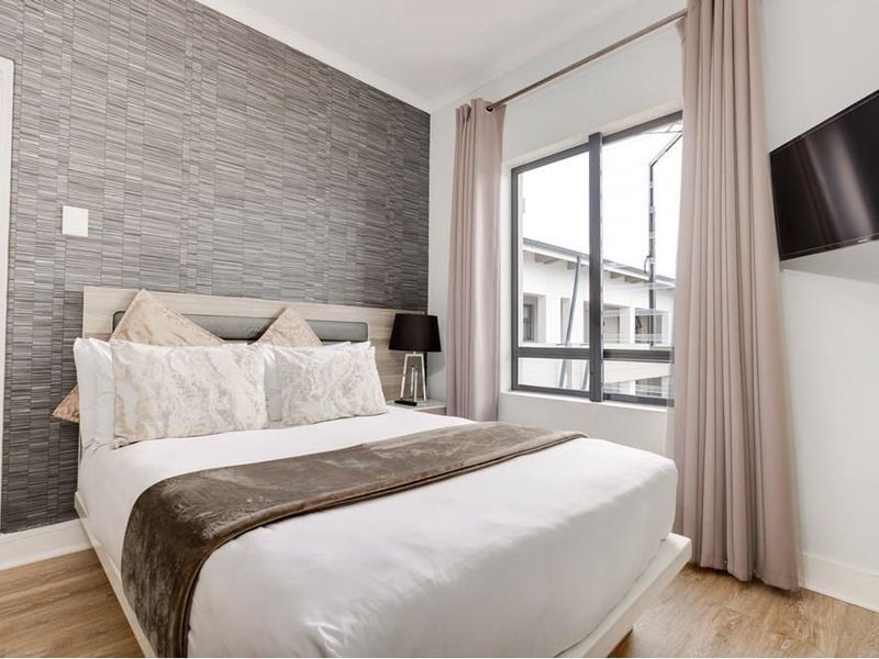 A well-maintained bedroom featuring modern textured wallpaper, laminate flooring, and a large window providing natural light.