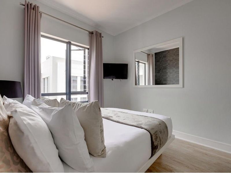 A well-maintained bedroom featuring light laminate flooring, neutral wall finishes, and a built-in wardrobe with modern aluminium window frames.