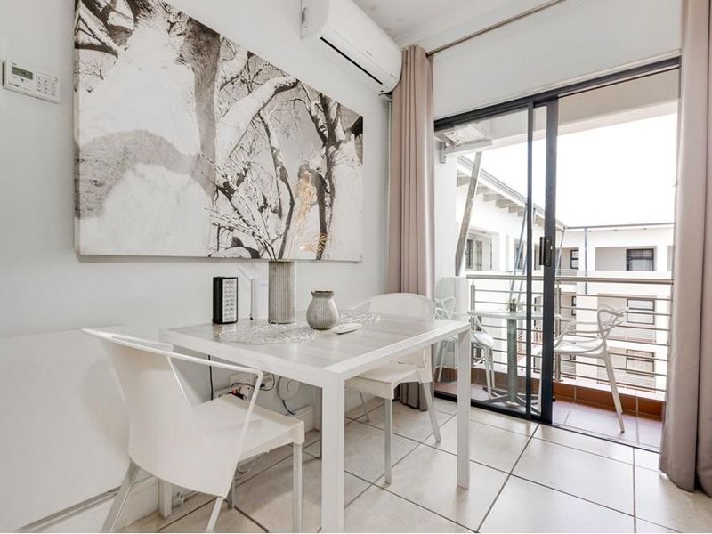 A bright living area featuring tiled flooring, a wall-mounted air conditioning unit, and direct access to a private balcony through sliding glass doors.