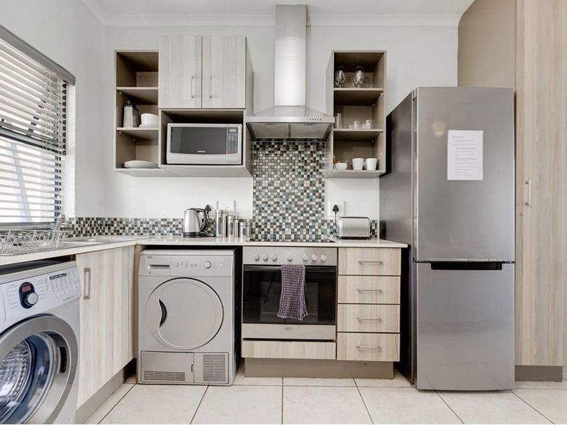 A modern, well-equipped kitchen featuring light wood-finish cabinetry, a mosaic tile backsplash, stainless steel appliances, and integrated laundry facilities.