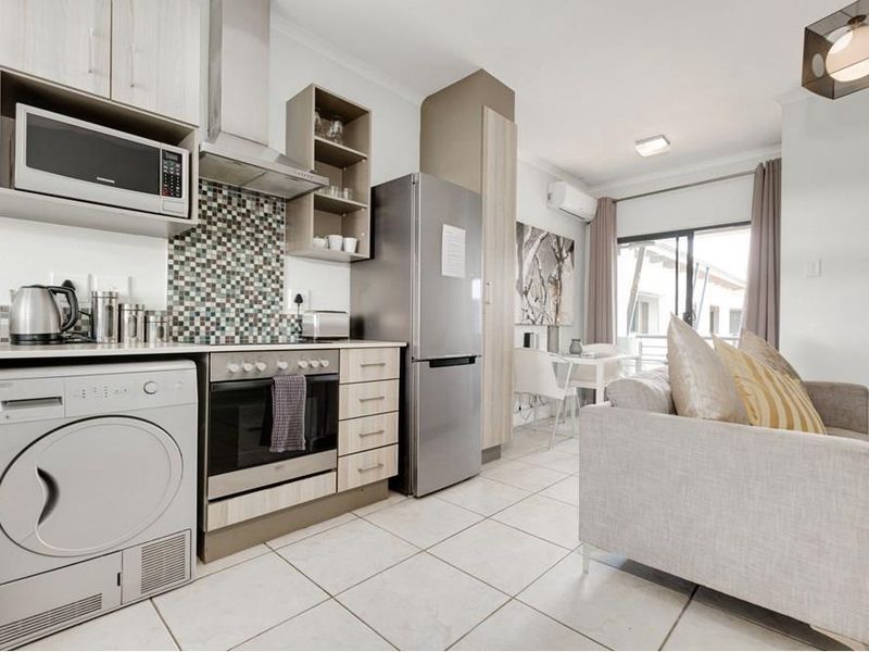 Modern open-plan living area featuring a well-equipped kitchen with built-in appliances, mosaic backsplash, and direct access to a balcony through sliding glass doors.