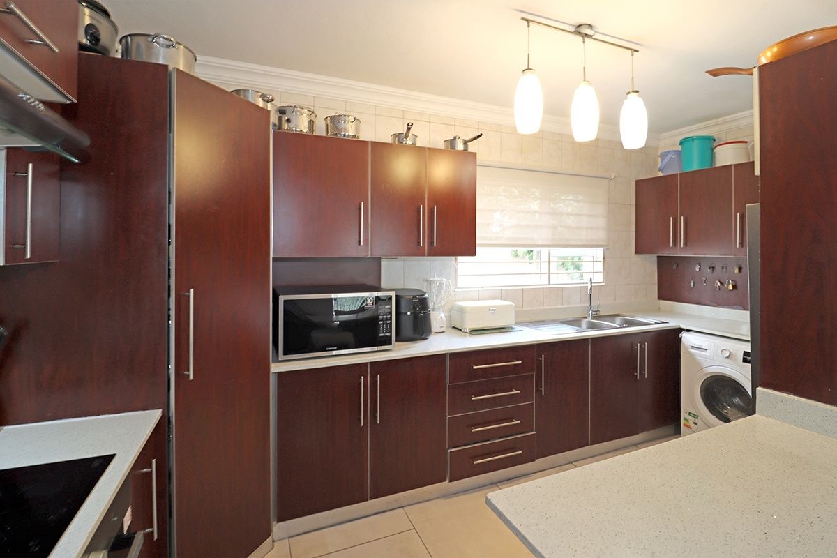 A functional kitchen featuring dark wood-finish cabinetry, light countertops, tiled backsplash, and integrated appliances, offering a practical layout for daily meal preparation.