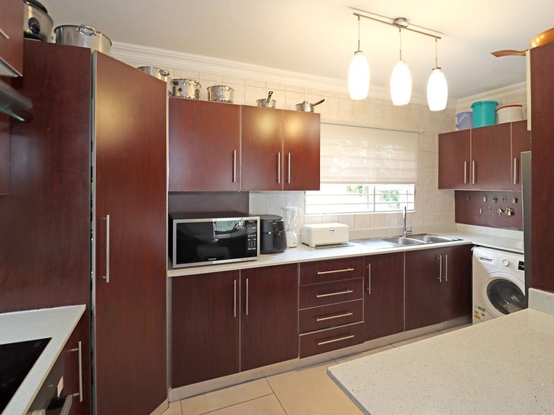 A functional kitchen featuring dark wood-finish cabinetry, light countertops, tiled backsplash, and integrated appliances, offering a practical layout for daily meal preparation.