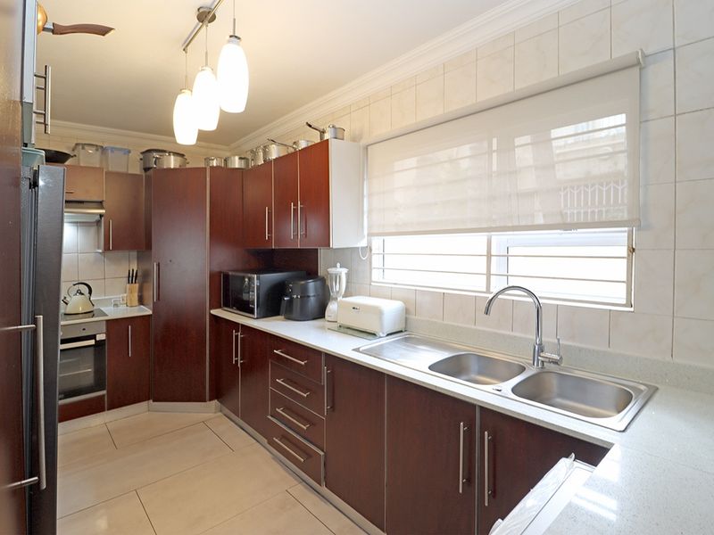 A functional kitchen featuring dark wood cabinetry, stone countertops, a double basin sink, and integrated appliances including an oven and hob.