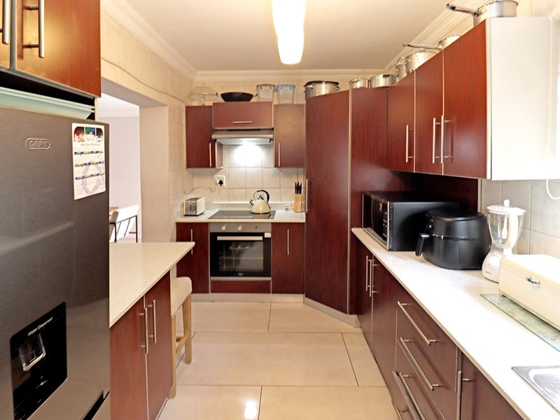 A functional kitchen featuring dark wood cabinetry, stone countertops, built-in oven and hob, and tiled flooring with a clean, practical layout.