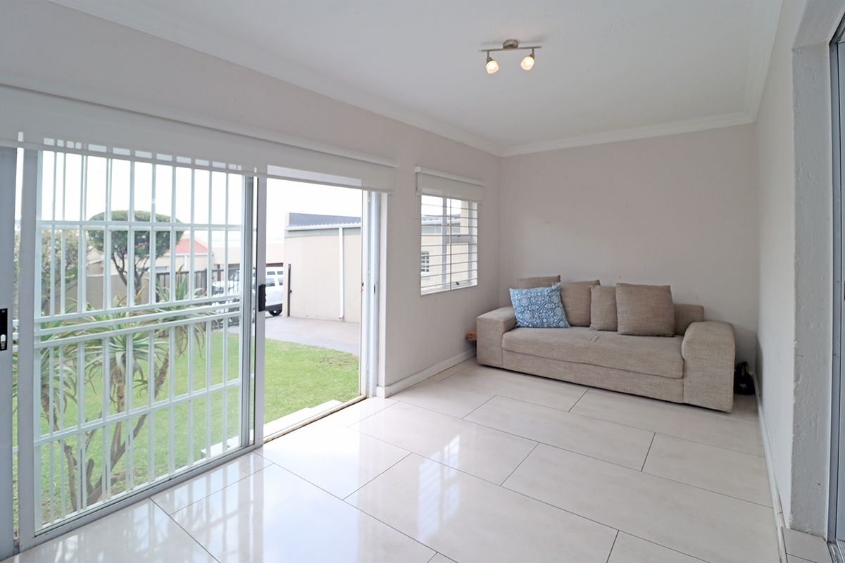 Bright living room featuring large sliding glass doors with security gates, neutral tiled flooring, and direct access to the garden area.