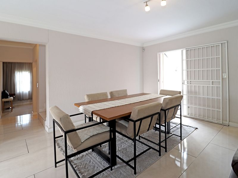 A bright dining room featuring neutral tiled flooring, ceiling cornice detailing, and a sliding security gate providing access to the outdoor area.