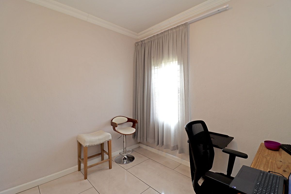 A functional bedroom space featuring neutral tiled flooring, cornice detailing, and a window fitted with a curtain rail.